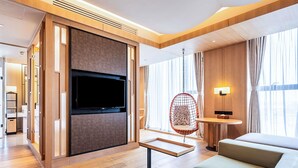 A modern hotel room with a large flat-screen TV mounted on a wooden panel, a hanging chair, a small round table, and a sofa. - Swissotel Hot Spring Hotel Xi'an Xinxing (Xi'an)