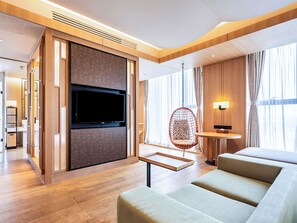 A modern hotel room with a large flat-screen TV mounted on a wooden panel, a hanging chair, a small round table, and a sofa. - Swissotel Hot Spring Hotel Xi'an Xinxing (Xi'an)