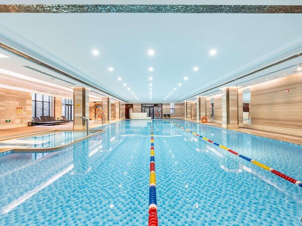 A large indoor swimming pool with clear lane dividers, a lifeguard chair, and a reception area with a sign indicating the pool's location. - Swissotel Hot Spring Hotel Xi'an Xinxing (Xi'an)