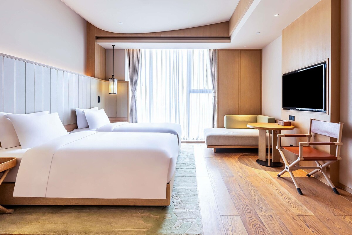 A hotel room with a large bed, a smaller bed, a TV, a desk, and a chair.