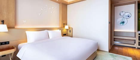 A modern hotel room with a large bed, a wooden headboard, a nightstand, a lamp, and a wall with butterfly and floral art.