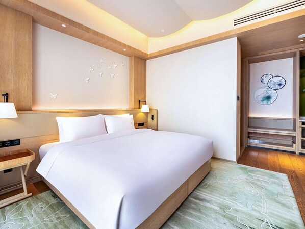 Una habitación de hotel moderna con una cama grande, un cabecero de madera, una mesita de noche, una lámpara y una pared decorada con arte floral y de mariposas.