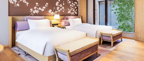 Una habitación de hotel moderna con dos camas, un cabecero de madera, una mesita de noche con lámpara, un ventanal con vistas a bambú y una pared decorativa con motivos florales.