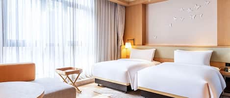 A hotel room with two beds, a sofa, a small table, and a large window with sheer curtains.