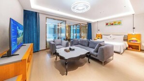 A modern hotel room with a sofa, coffee table, TV, and a bed.