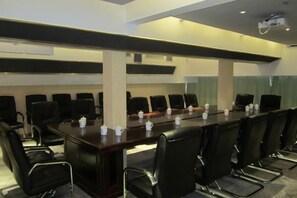 Un salón de conferencias con una larga mesa, varias sillas y un proyector.