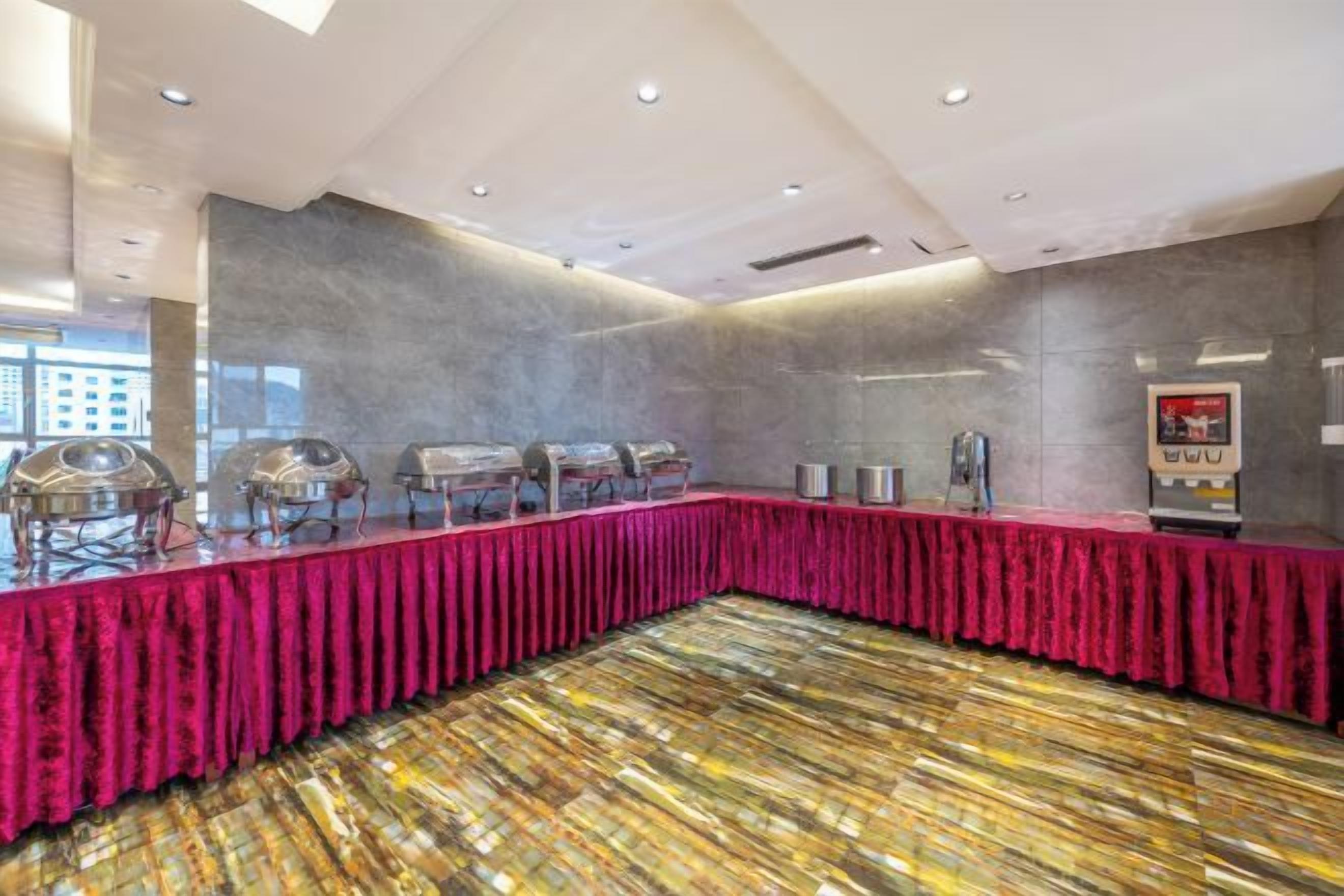 A conference room with a long table covered in a red cloth, equipped with multiple food service stations.