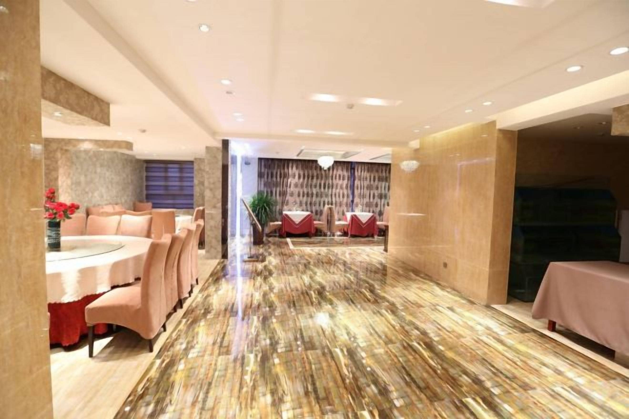 A hotel lobby with a marble floor, round tables, and chairs, leading to a seating area with red upholstered chairs.