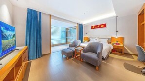 A hotel room with a bed, a TV, a desk, a chair, a small table, and a window with curtains.
