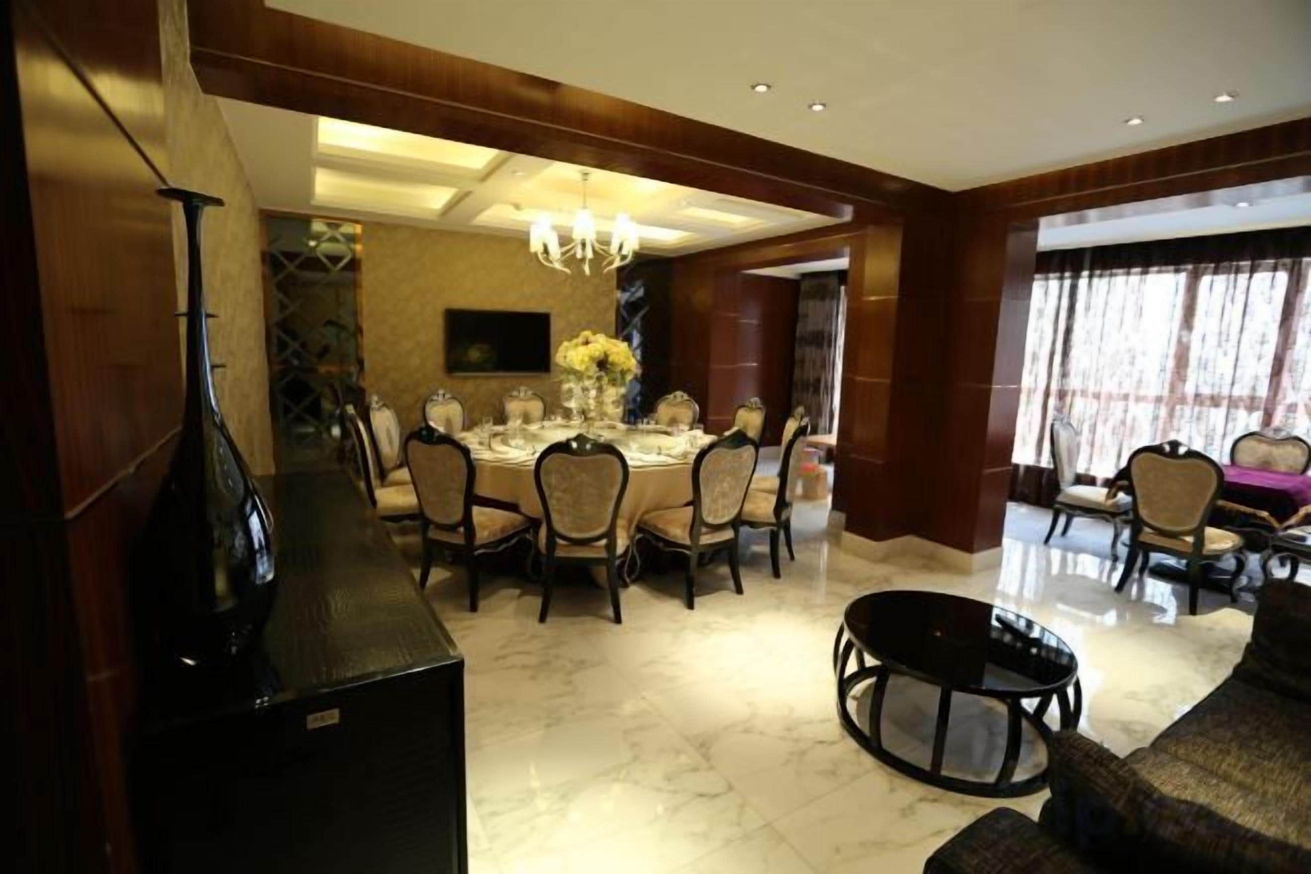 Un comedor con una mesa redonda, sillas y una araña. Se observa un sofá y un televisor al fondo.