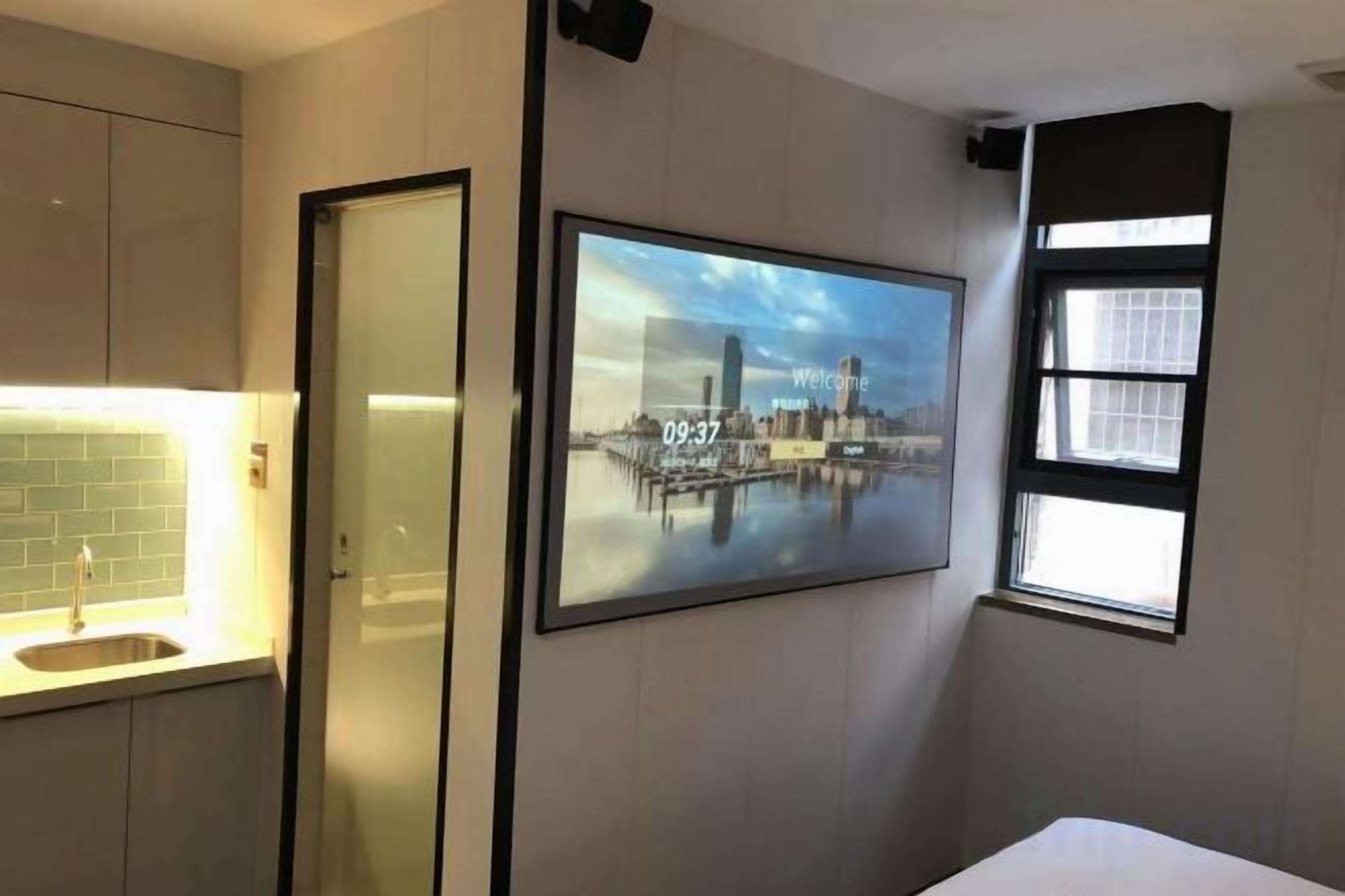 Ein Hotelzimmer mit einem Bett, einem am Wand montierten Fernseher, einem Fenster und einer Tür.