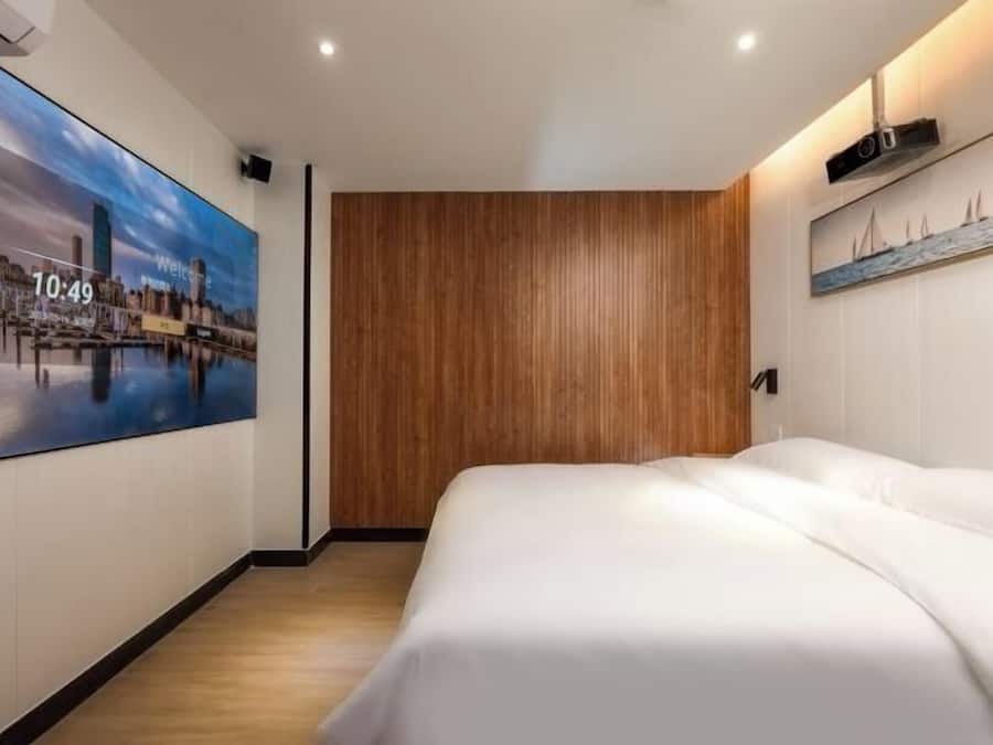 Quarto de hotel com cama, parede de painel de madeira, pintura de paisagem urbana e relógio marcando 10:49.