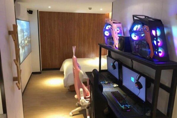 Una habitación de hotel con una cama, un escritorio con una computadora y computadoras para juegos con iluminación RGB.