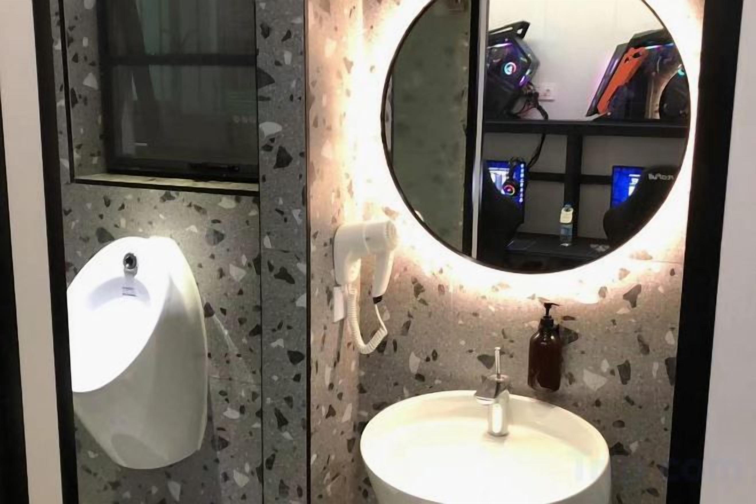 A restroom with a urinal, a sink, a mirror, and a soap dispenser.