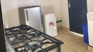 Una cocina con estufa a gas, dos refrigeradores, un mueble negro con puertas de vidrio y un bote de basura azul.
