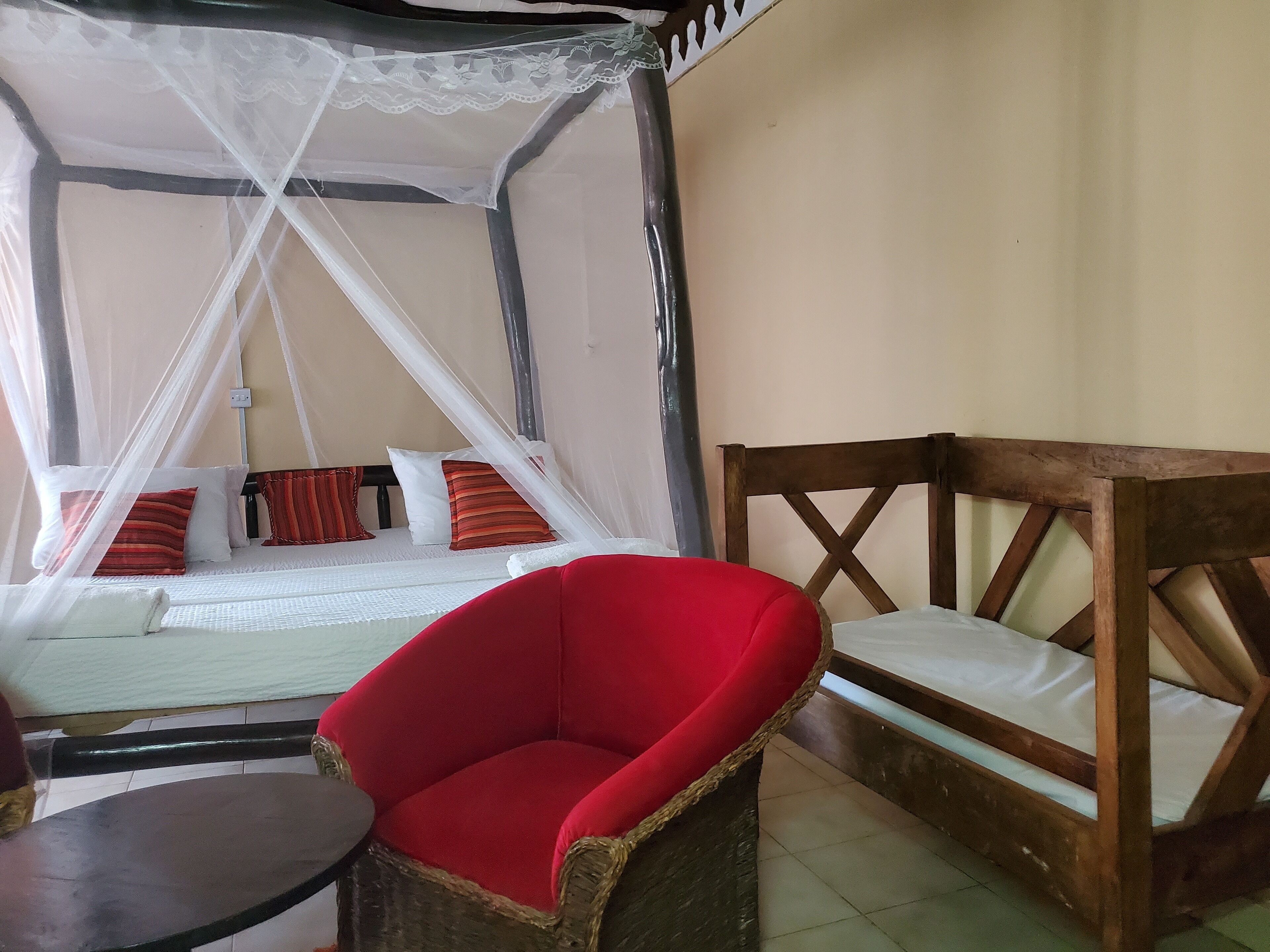 A room with a bed under a canopy, a red chair, and a wooden bench.