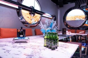 Una zona de bar con un espejo circular, una botella y una pila de latas sobre una encimera de mármol.