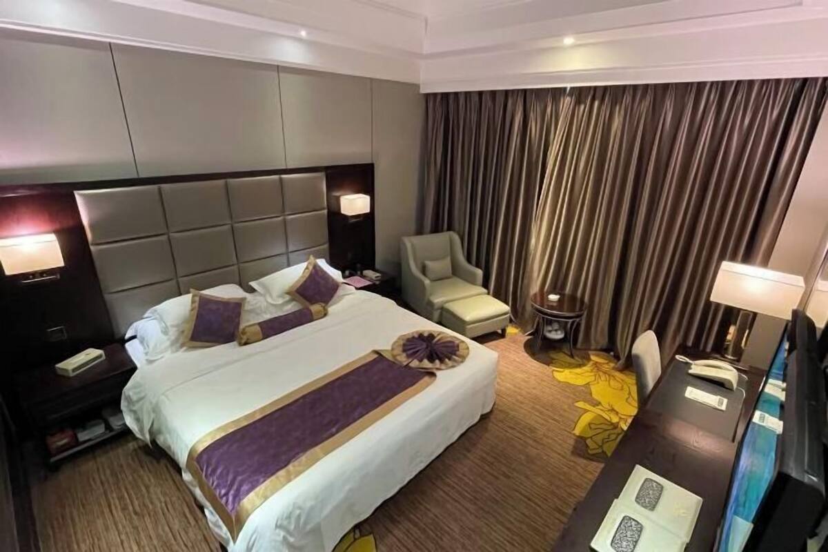 A hotel room with a large bed, a desk, a chair, a nightstand, and a curtain.
