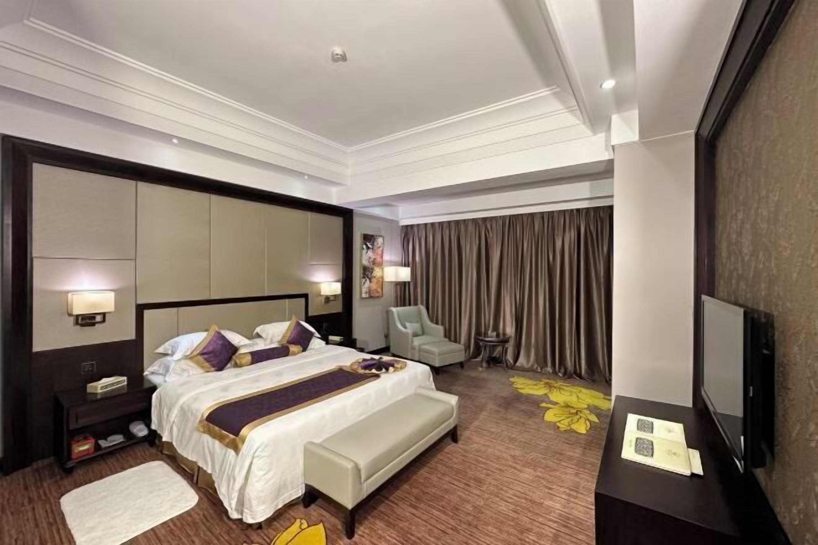 A hotel room with a large bed, bedside tables, a TV, a chair, and a small table.