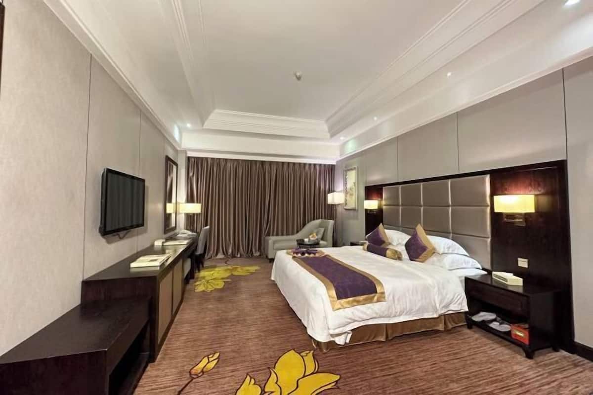 A hotel room with a large bed, a desk, a television, and a seating area.
