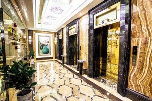 Um saguão de hotel com piso de mármore, balcão de recepção e uma grande obra de arte emoldurada na parede.