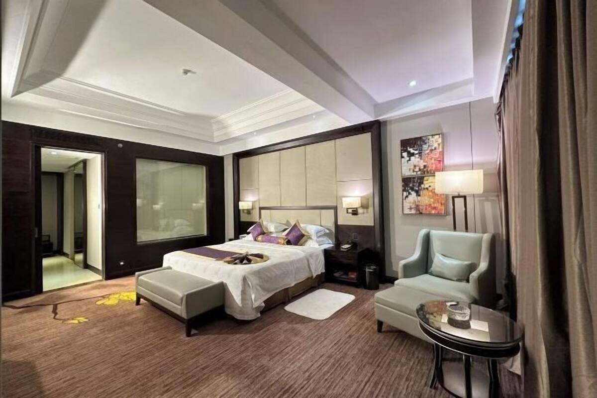 A hotel room with a bed, a seating area, a small table, and a large window.