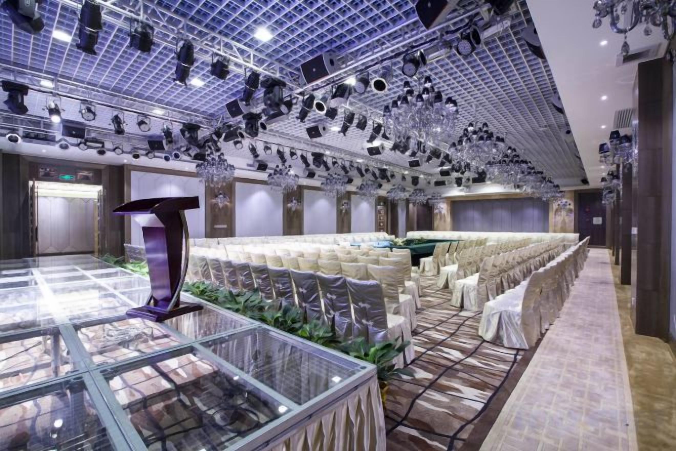 Une salle de banquet spacieuse, avec des rangées de chaises blanches, une table centrale et une vitrine.