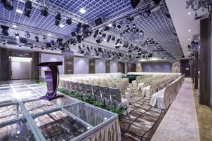 Un amplio salón de banquetes con filas de sillas blancas, una mesa central y una vitrina de vidrio.