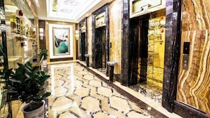 A hallway with marble flooring, black and gold elevators, and a ceiling with a floral pattern. - Jiahua Hotel (Puning)