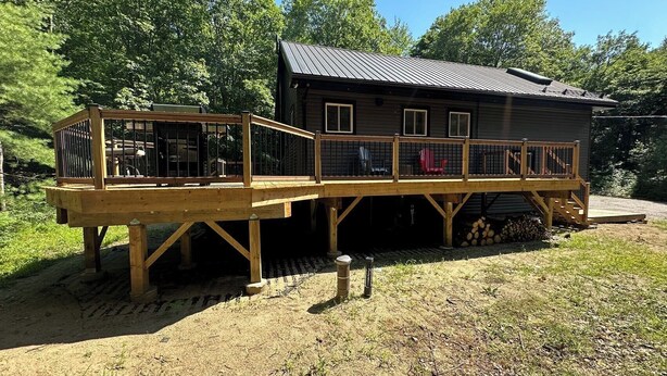 Eine Holzhütte mit einer Holzterrasse und einem Metalldach, umgeben von Bäumen.