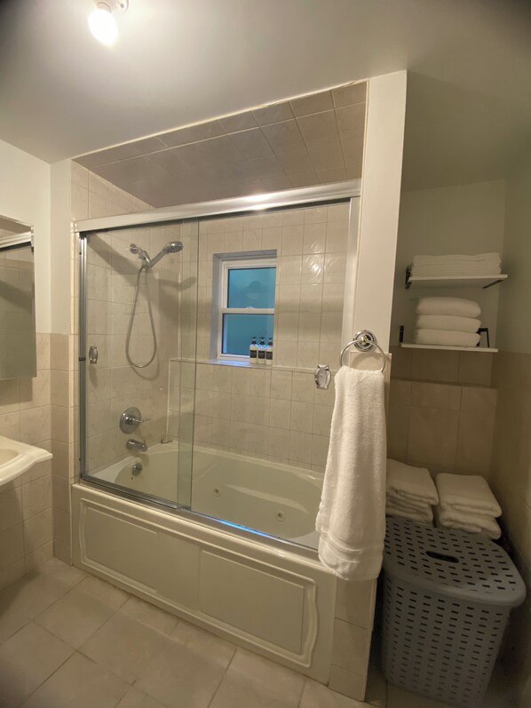 Un baño con ducha de vidrio, bañera, ventana y estante con toallas.