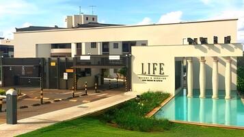 Um edifício moderno com piscina, entrada fechada por portão e um letreiro que diz 'LIFE'.