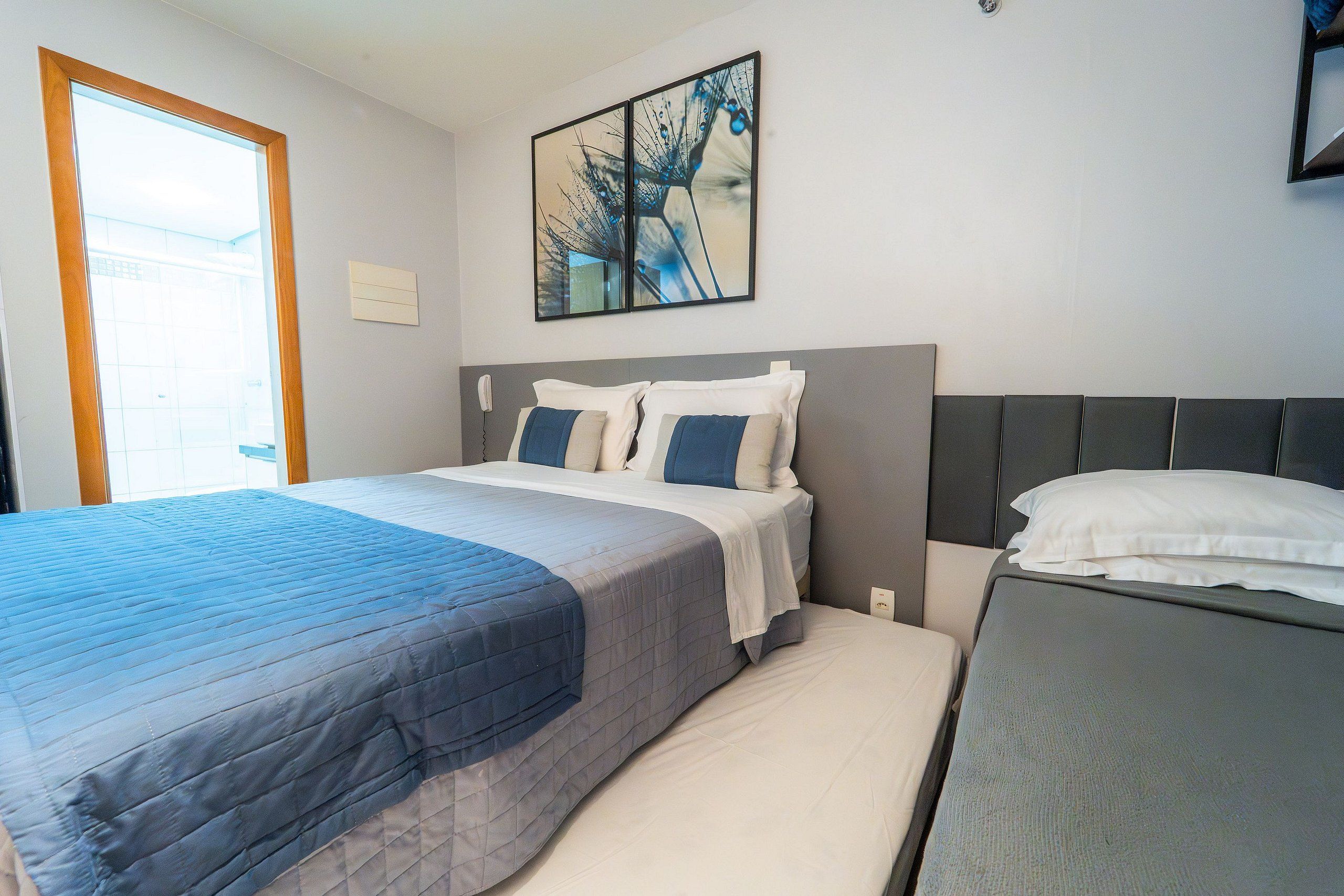 Un dormitorio con cama, mesita de noche, una obra de arte en la pared y ventana.