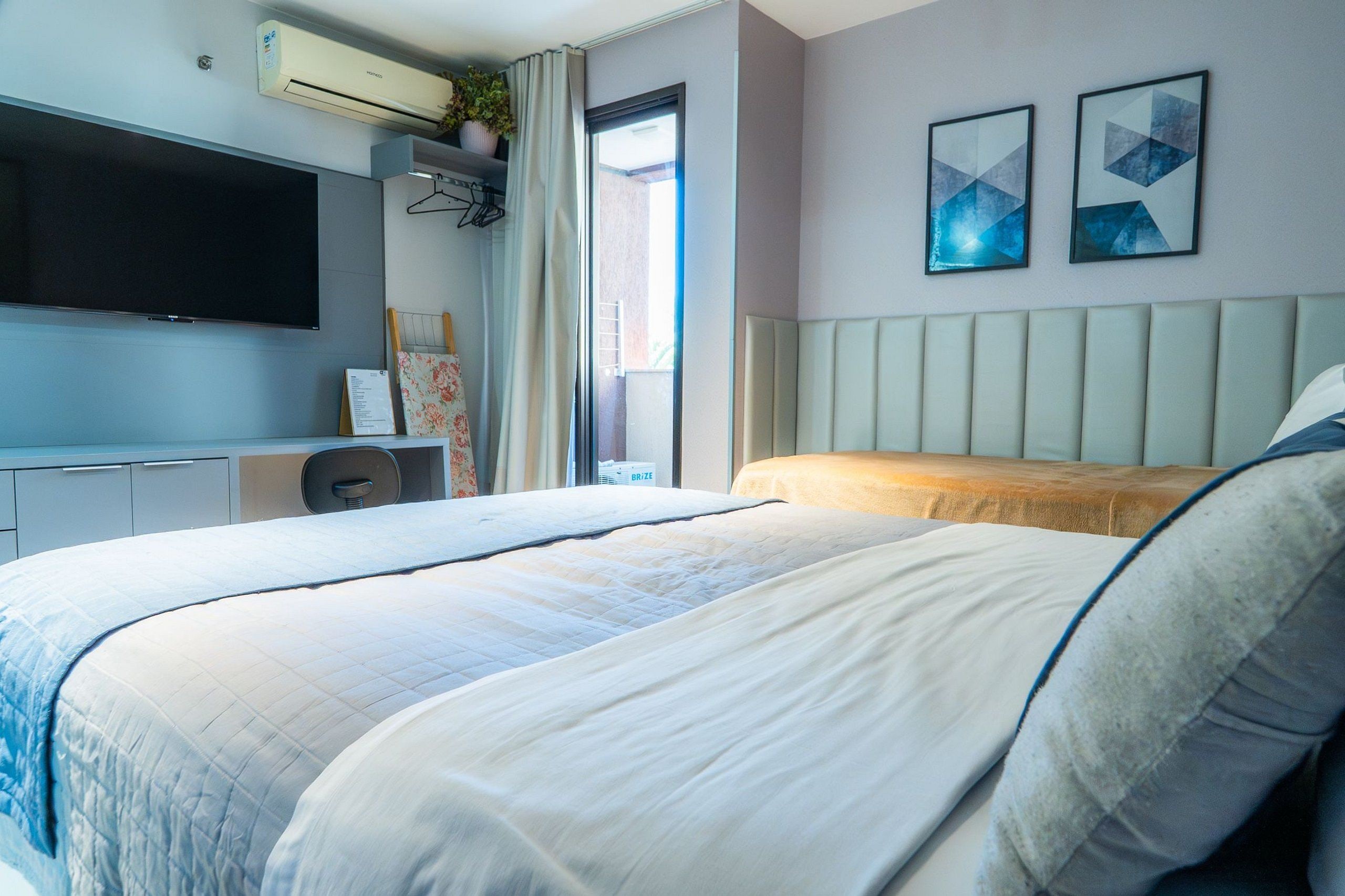 A modern hotel room with a large bed, a flat-screen TV, a desk, and a window with curtains.