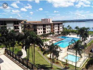 A hotel with multiple floors, a swimming pool, and palm trees. - Life resort (Brasília)