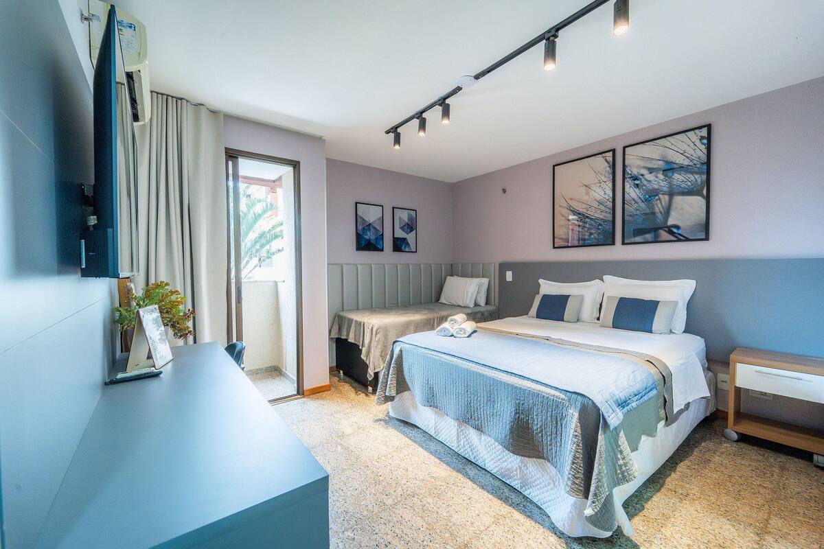 A modern hotel room with a bed, a desk, a chair, a TV, and a window.