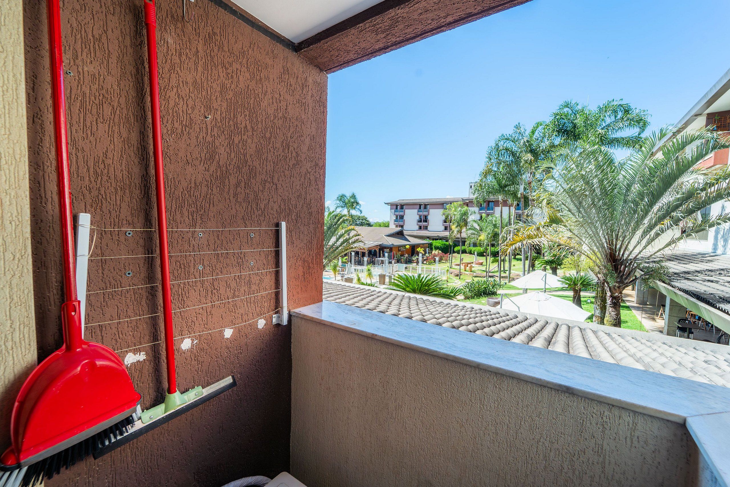 Un balcón con vista a un patio, una escoba roja y una rejilla de metal.
