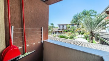 Un balcón con vista a un patio, una escoba roja y una rejilla de metal.