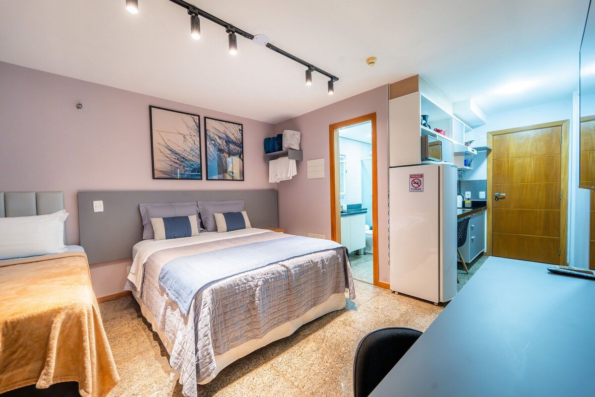 A bedroom with two beds, a desk, and a kitchenette.