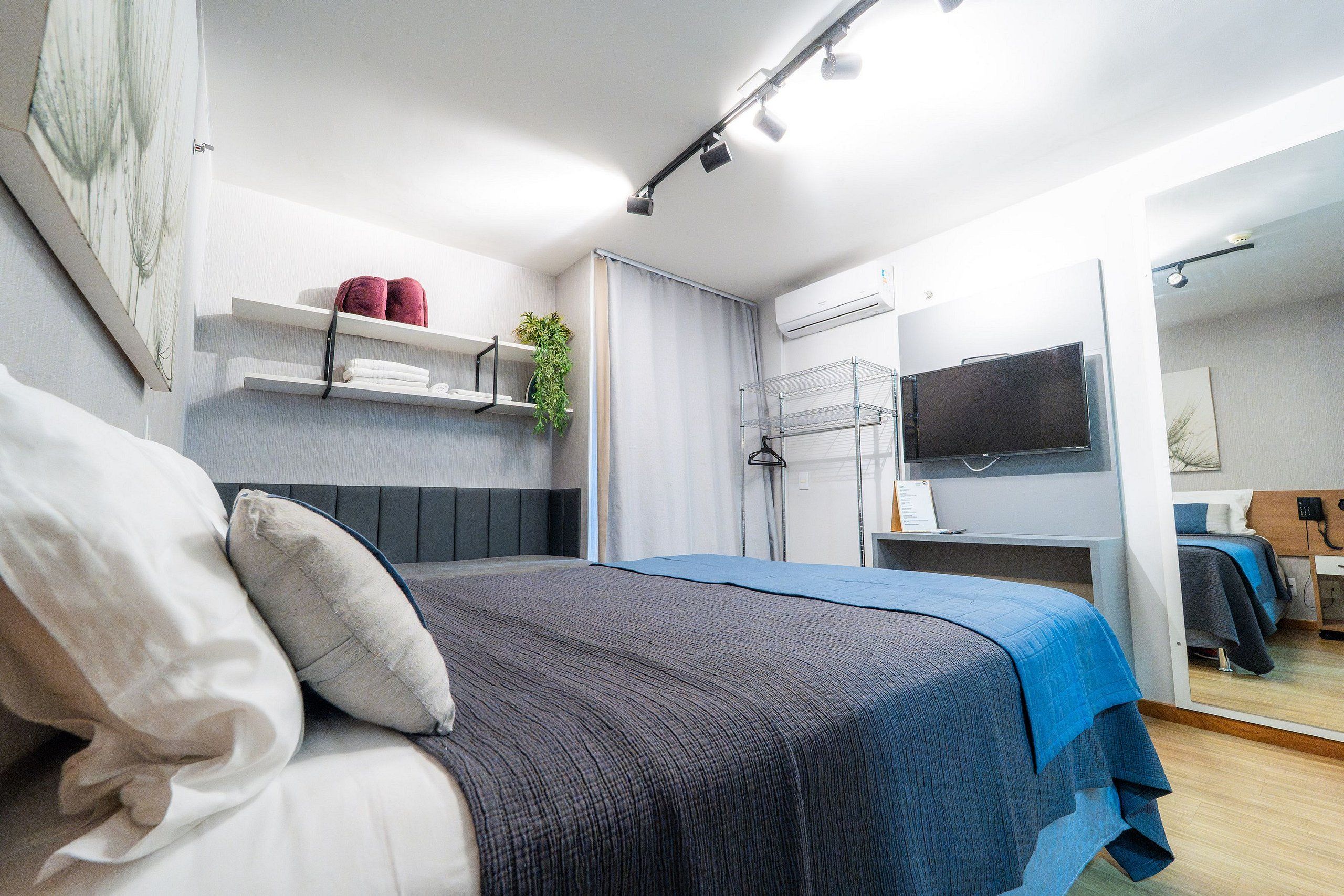 Un dormitorio moderno con cama, televisor, estante con toallas y una planta.