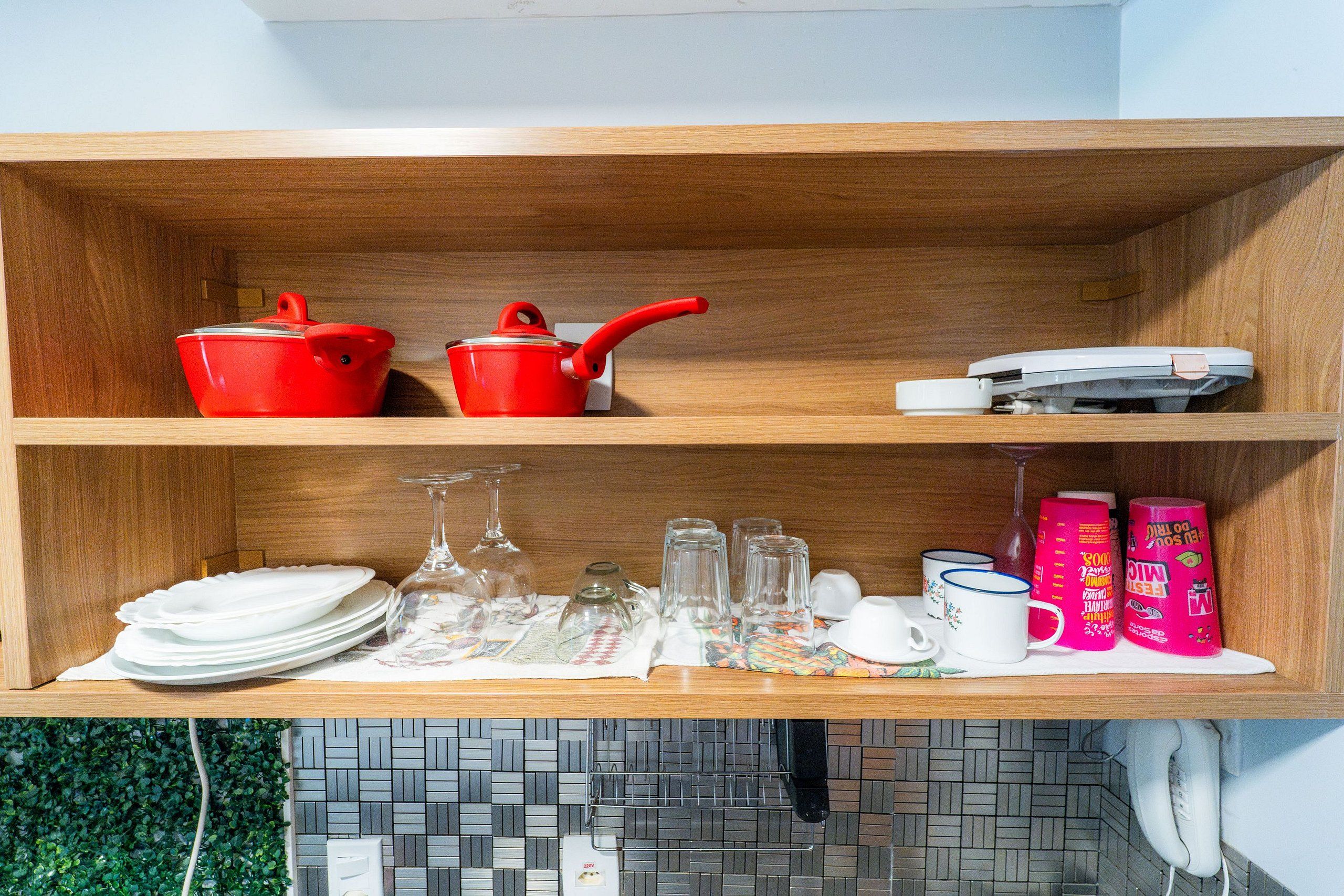 A kitchen shelf with red cookware, a white phone, and various glassware.