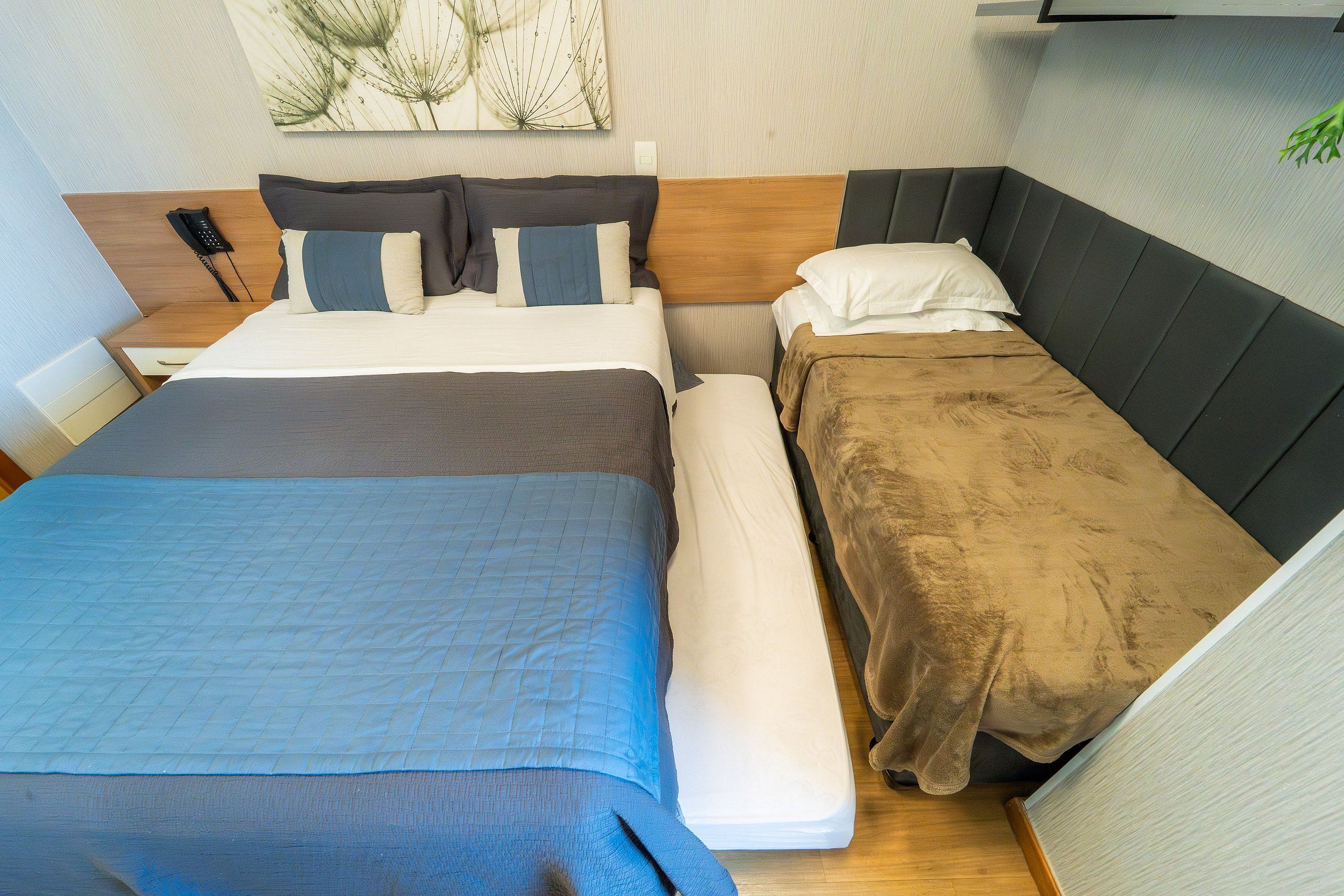 Habitación de hotel con dos camas, cabecero de madera, mesita de noche con lámpara y teléfono en la pared.