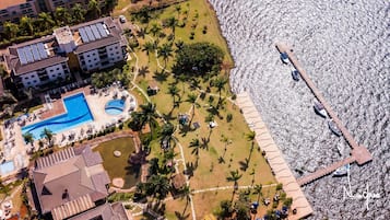 Luchtbeeld van een resort met een zwembad, een strandgedeelte en een steiger met boten.