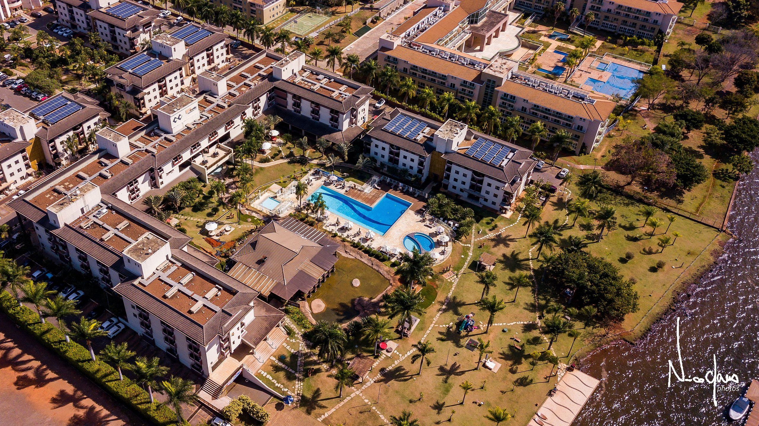 Vista aérea de um conjunto residencial com vários edifícios, uma piscina central e áreas verdes ao redor.