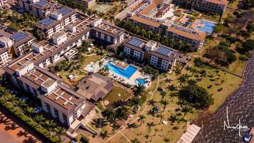Vista aérea de um conjunto residencial com vários edifícios, uma piscina central e áreas verdes ao redor.