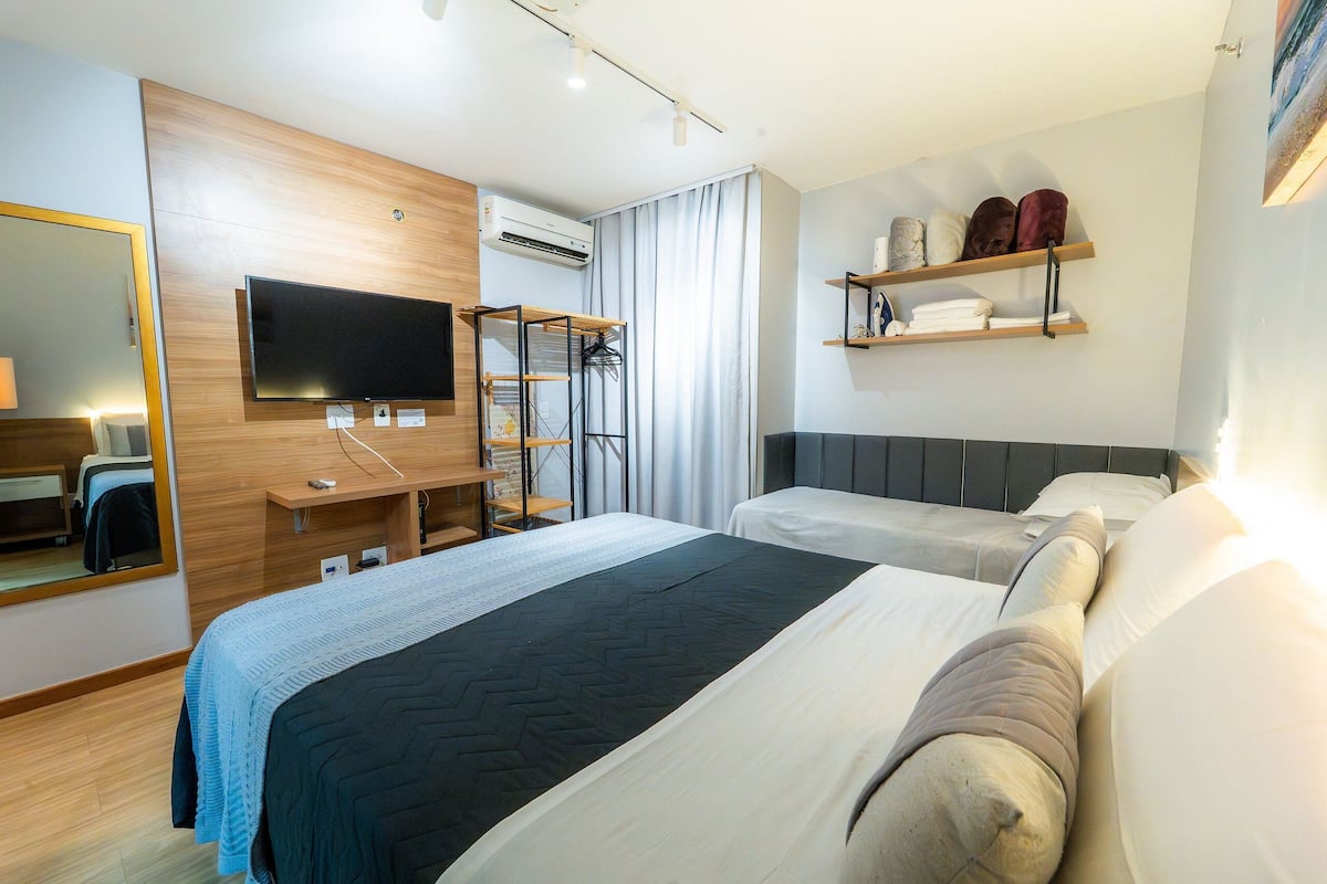 A modern hotel room with a large bed, a TV, a desk, and a wardrobe.