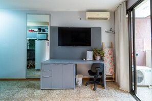 A compact room with a desk, chair, TV, air conditioning unit, and a sliding door leading to a balcony. - Life resort (Brasília)