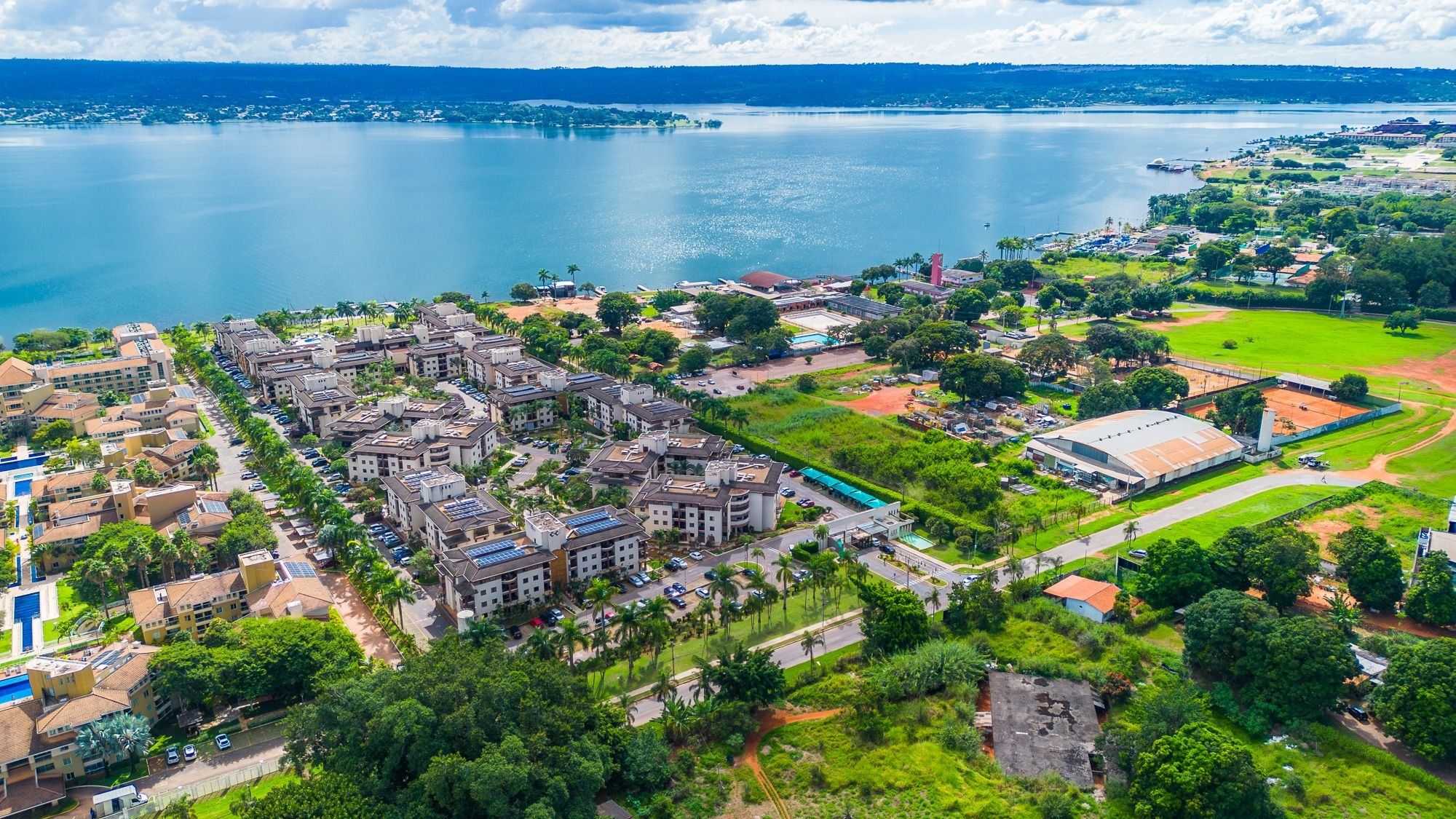 An aerial view of a coastal town with residential buildings, a large body of water, and a sports field.