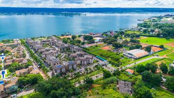 An aerial view of a coastal town with residential buildings, a large body of water, and a sports field.