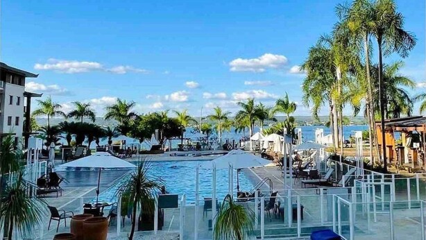A pool area with lounge chairs and palm trees, overlooking a body of water. - Life resort (Brasília)